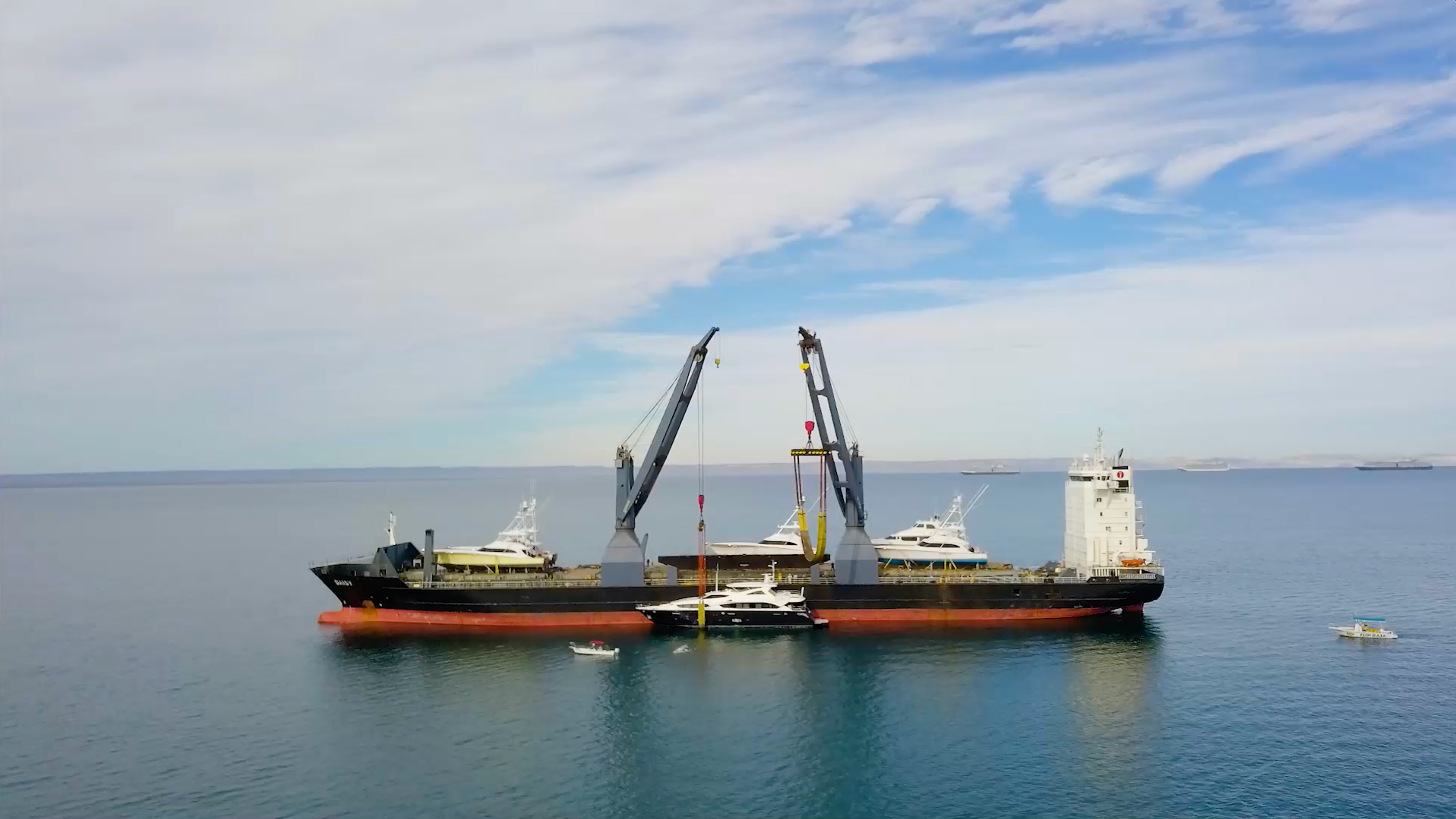 Yachts being loaded aboard a transport vessel on the water